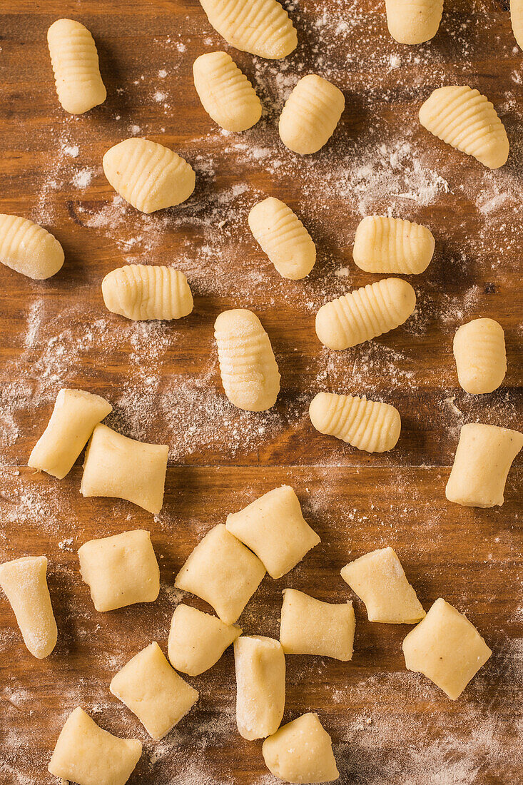 From above top view of uncooked gnocchi placed in rows on lumber table during lunch preparation at home