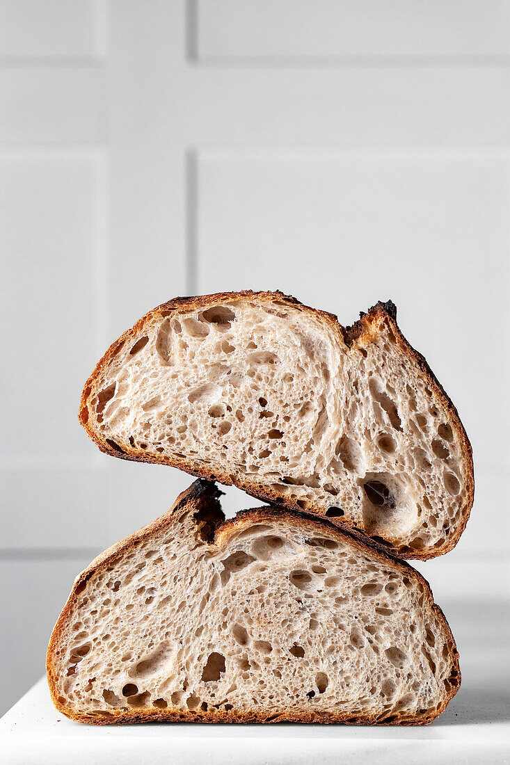 Halves of tasty sourdough bread with brown crust placed on table against white backdrop