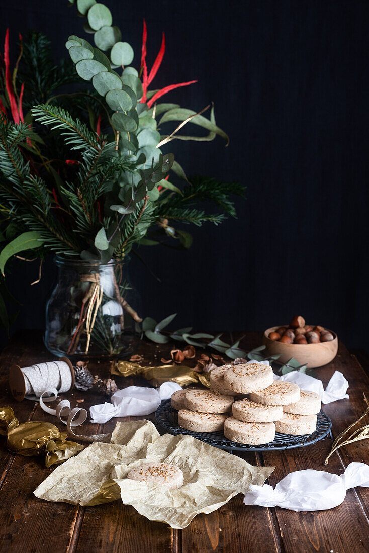 Pile of appetizing sweet shortbread cookies with hazelnuts served on plate on wooden table with festive wrapping paper and ribbons for Christmas celebration