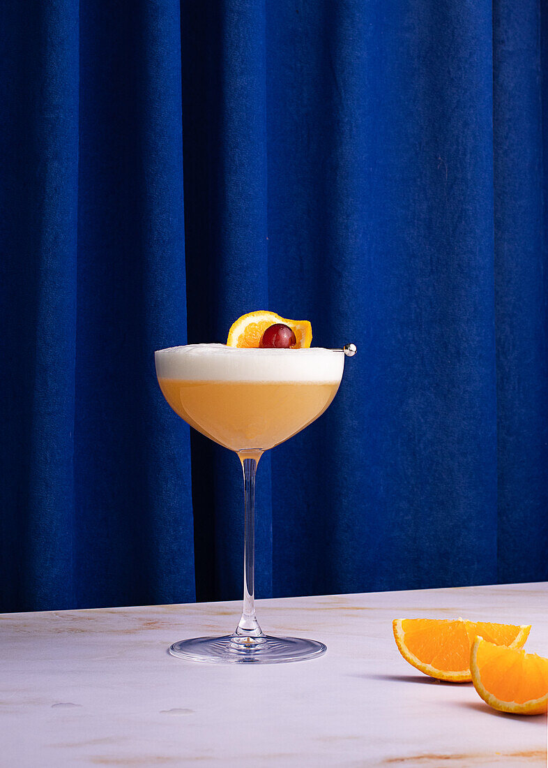 Whiskey-Sour-Cocktail im Glas auf buntem blauem Vorhanghintergrund im Studio