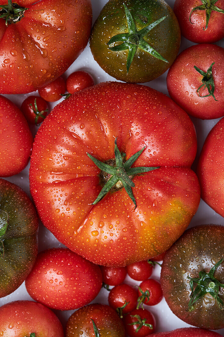 From above of appetizing fresh ripe tomatoes with drops of water near branch with green leaves