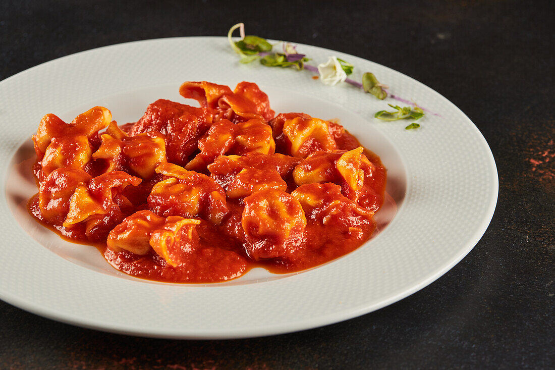 Blick von oben auf leckere Fleischravioli mit Ragu-Bolognese-Sauce, serviert auf einem Teller mit Sprossen auf einem dunklen Tisch im Restaurant