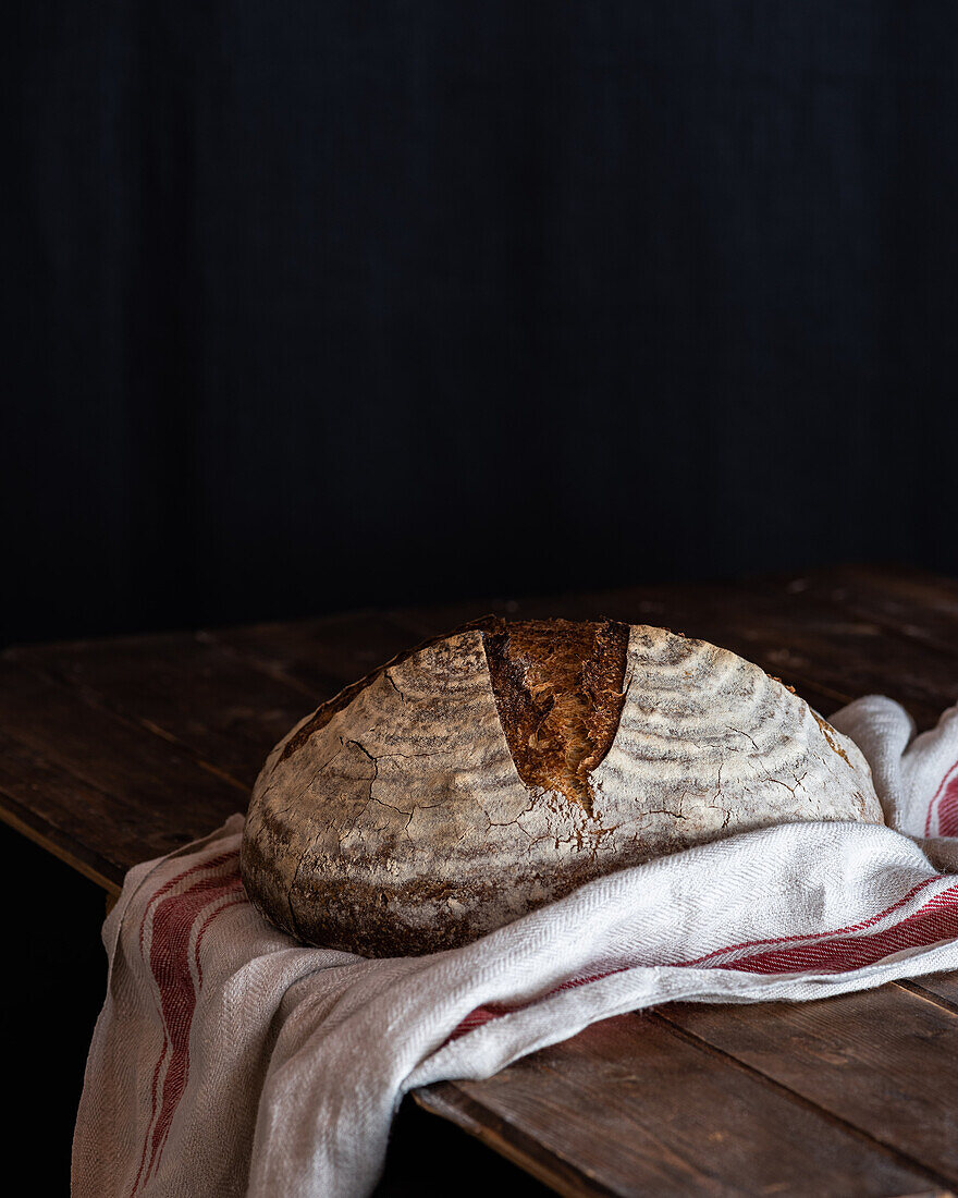 Homemade sourdough bread loaf with crispy crust on wooden rustic board on black background