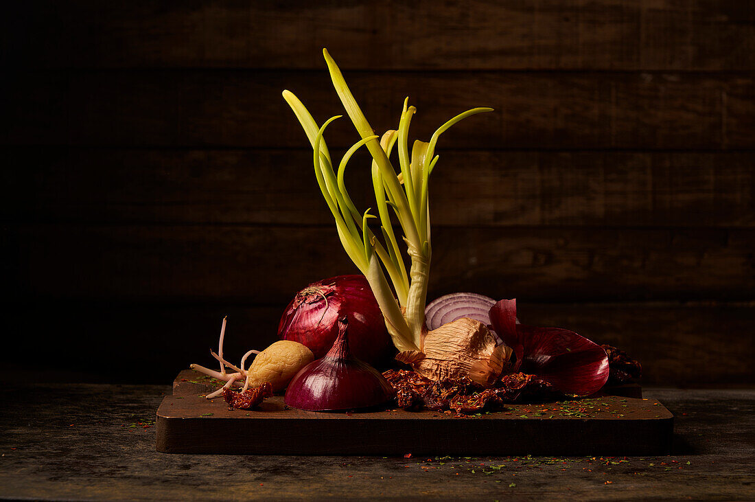 Still life composition with old geminated onion bulb and potato tuber with sprouts placed on wooden cutting board with dried tomatoes