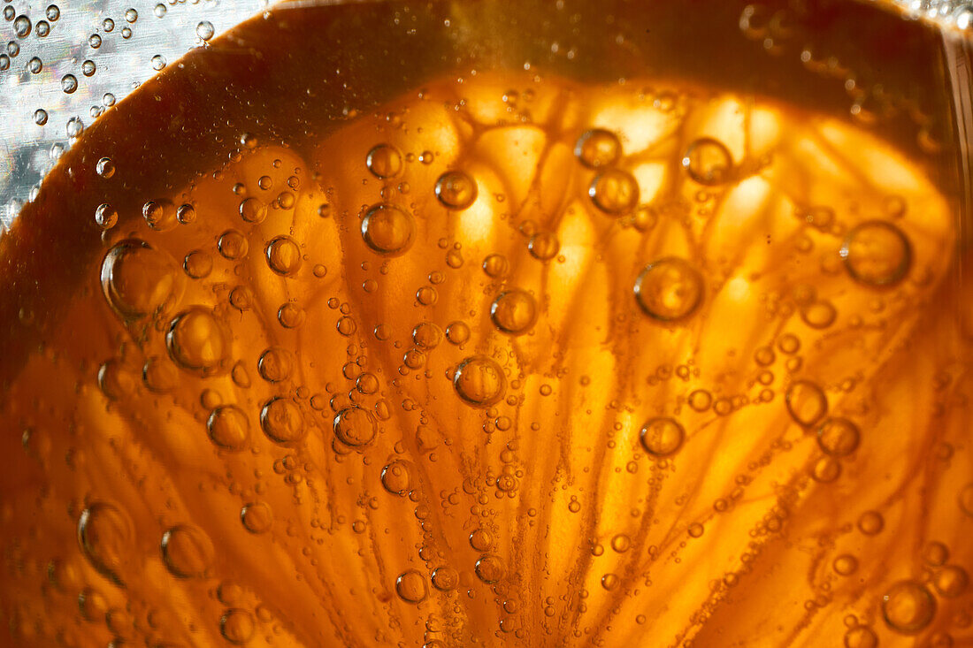 Close-up gin and tonic cocktail with slice of fresh orange bubbling in glass