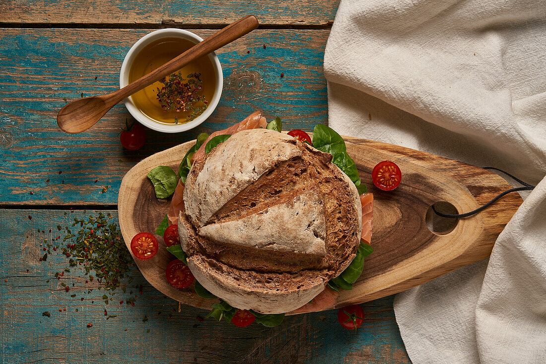 Draufsicht auf selbstgebackenes Sauerteigbrot mit Lachs, serviert auf einem hölzernen Schneidebrett mit Kirschtomaten auf einem schäbigen Tisch