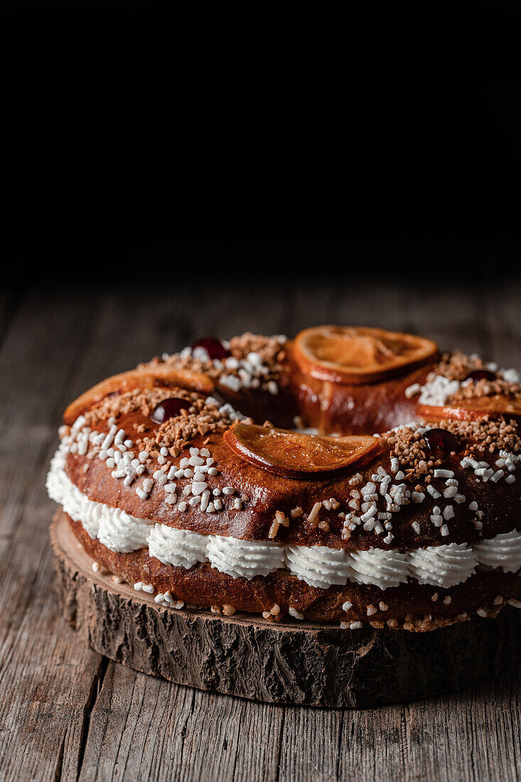 Königskuchen mit Sahne und Streuseln, dekoriert mit Orangenscheiben und Kirschen, auf Holztisch gestellt