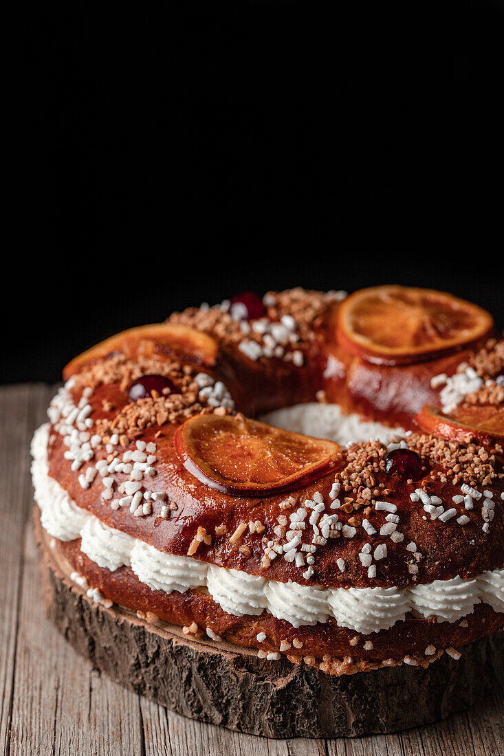 Königskuchen mit Sahne und Streuseln, dekoriert mit Orangenscheiben und Kirschen, auf Holztisch gestellt