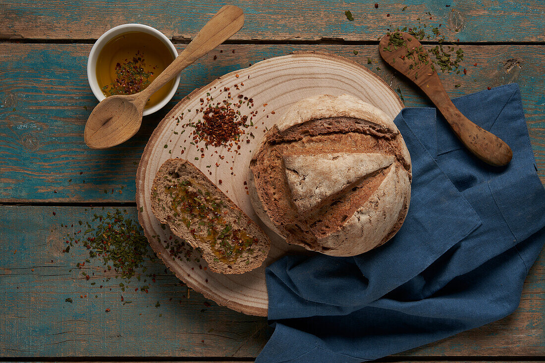 Top view of slice and loaf of baked bread served on round wooden chopping board with flavoring in light kitchen