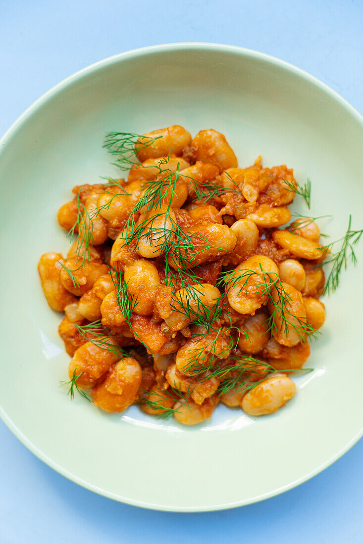 From above of delicious traditional Greek giant naked beans in tomato sauce served in plate on gray background in kitchen