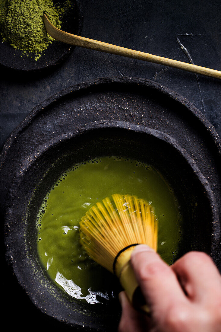 From above crop hand holding of traditional Japanese matcha with tea whisk in stone bowl for traditional oriental ceremony