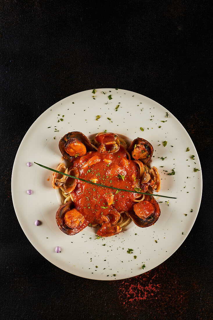 Nahaufnahme von Meeresfrüchtespaghetti mit Tomatensoße, die auf einem Teller auf schwarzem Hintergrund in einem Restaurant serviert werden