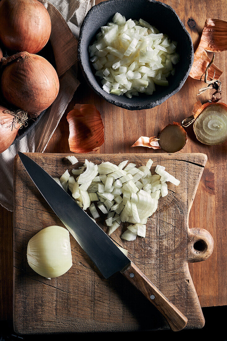 Top view of rustic bowl with pieces of cut onion placed near knife on lumber table in kitchen