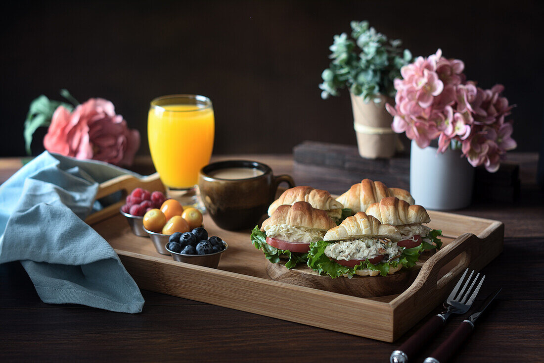 Delicious croissant sandwiches with vegetables served on tray with cappuccino and orange juice prepared for French breakfast and placed on wooden table