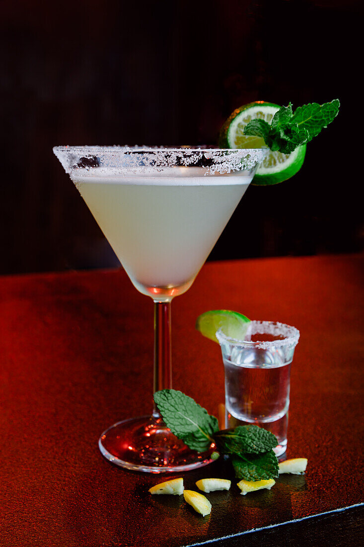 Crystal glass of alcoholic cocktail Margarita consisting of tequila orange liqueur and lime juice served with salt on rim of glass and mint leaf