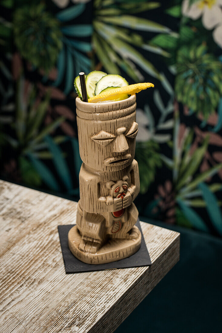 Traditionelle skulpturale Tiki-Tasse mit alkoholischem Getränk und Strohhalm auf einem Holztisch