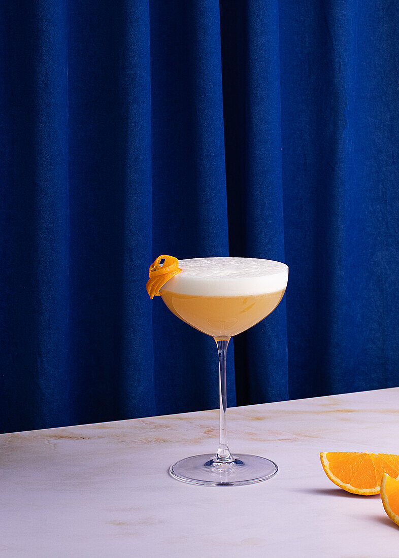 Whiskey sour cocktail in glass on colorful blue curtain background in studio