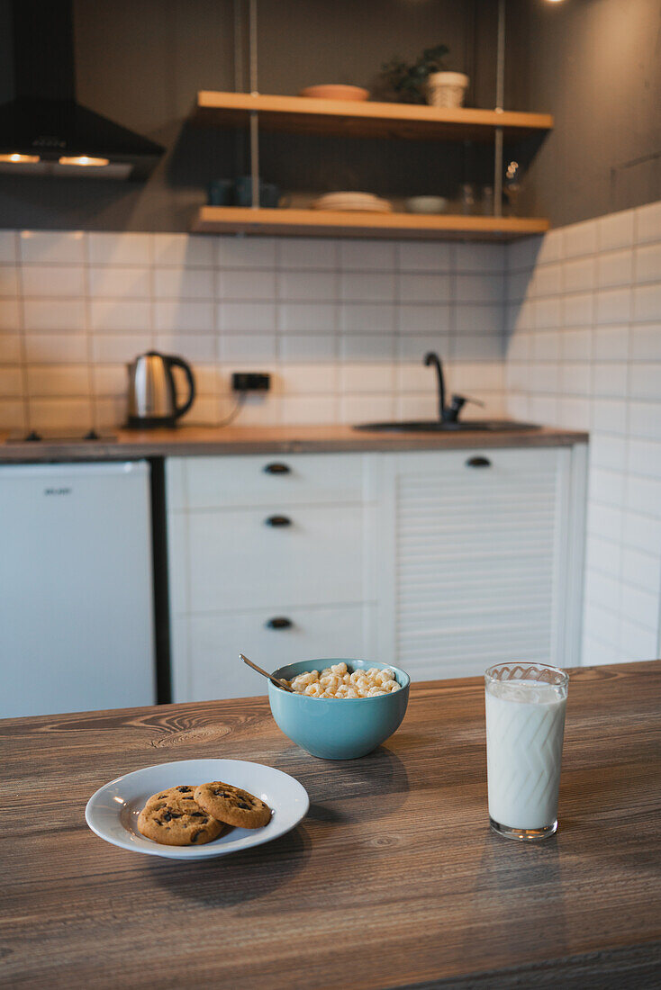 Plate with tasty oatmeal biscuits with chocolate chips against glass of milk on wooden table