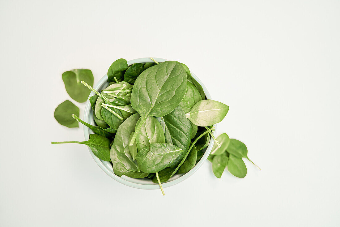 Top view of green spinach foliage with veins and stems in bowl on white surface