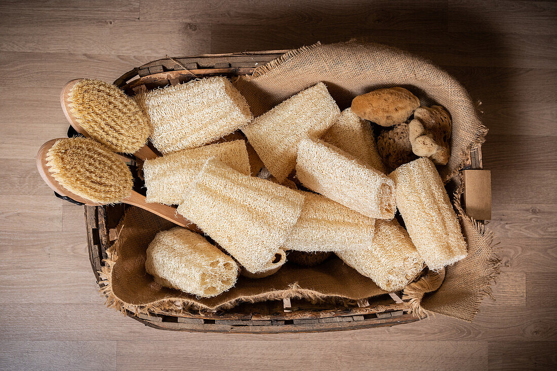 Draufsicht auf einen Holzkorb auf dem Boden, gefüllt mit Bürsten und abfallfreien natürlichen Luffaschwämmen