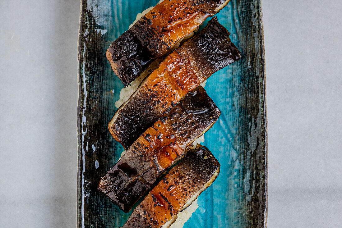 Grilled smoked eel nigiri over blue ceramic plate