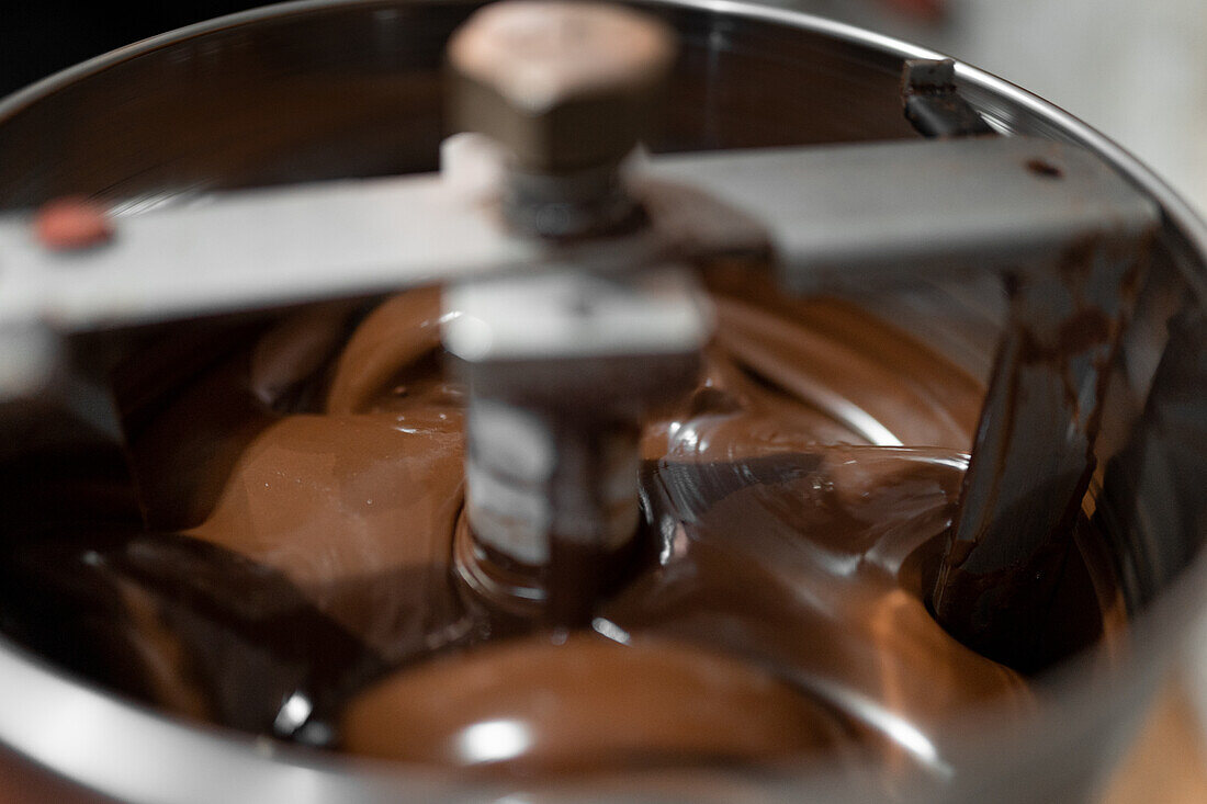 High angle closeup of shiny dark chocolate melting and crystallizing in tempering machine on chocolate production