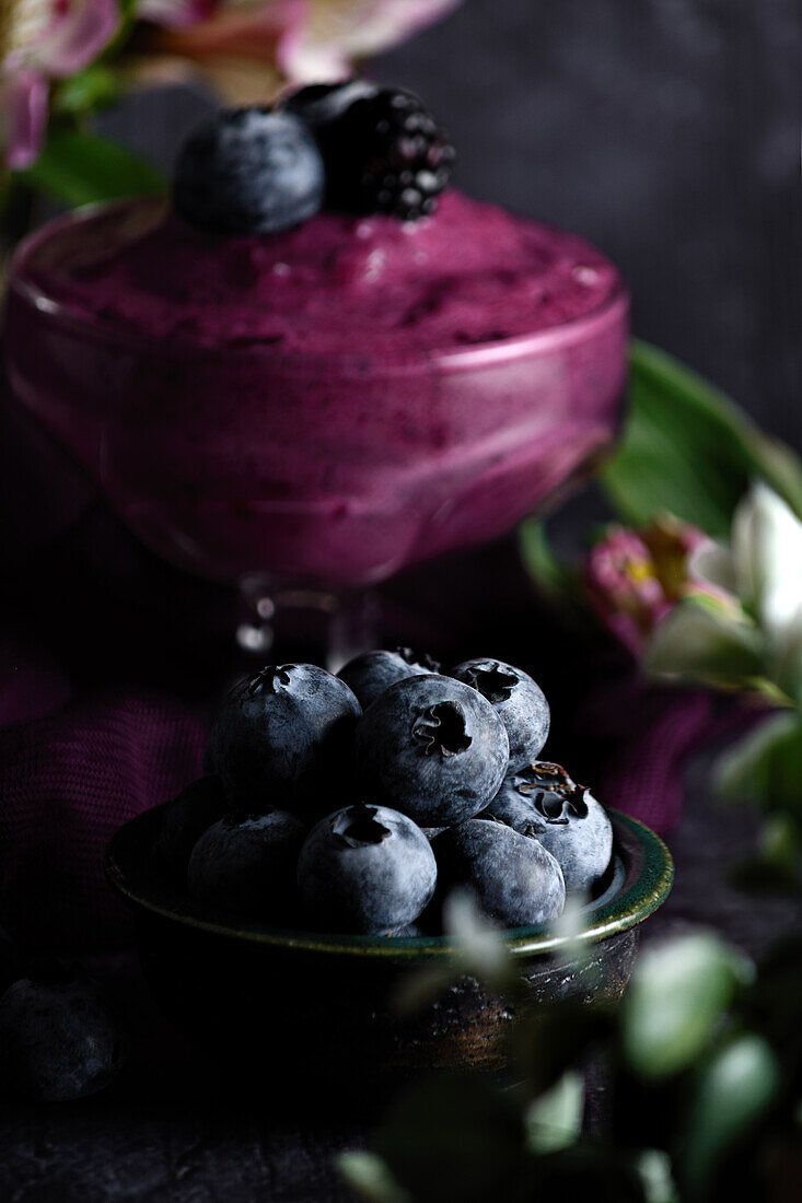 Nahaufnahme eines Haufens reifer Blaubeeren in einer Schüssel auf einem schwarzen Tisch mit lila Tuch