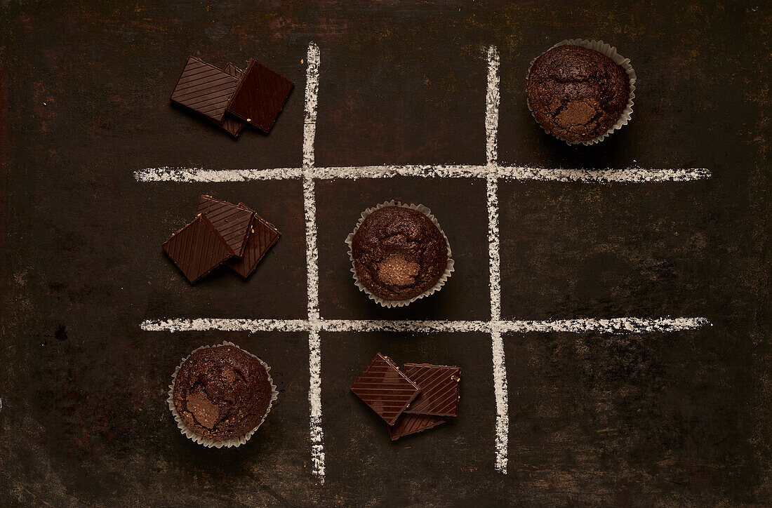 Top view of edible Tic tac toe game with baked muffins and sweet chocolate representing noughts and crosses placed on black background