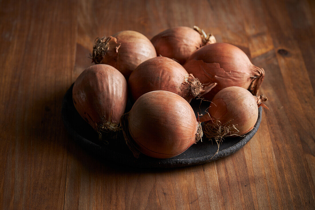 High angle of bunch of fresh unpeeled onions placed on plate on timber table