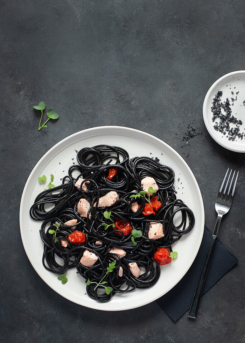 From above black ink spaghetti with salmon in ceramic plate on dark background