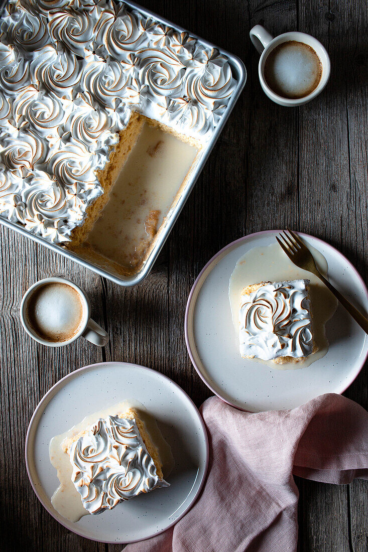 Von oben gesehen drei Milchkuchen in einer Auflaufform und Teller mit Tassen mit starkem Kaffee auf einem Holztisch