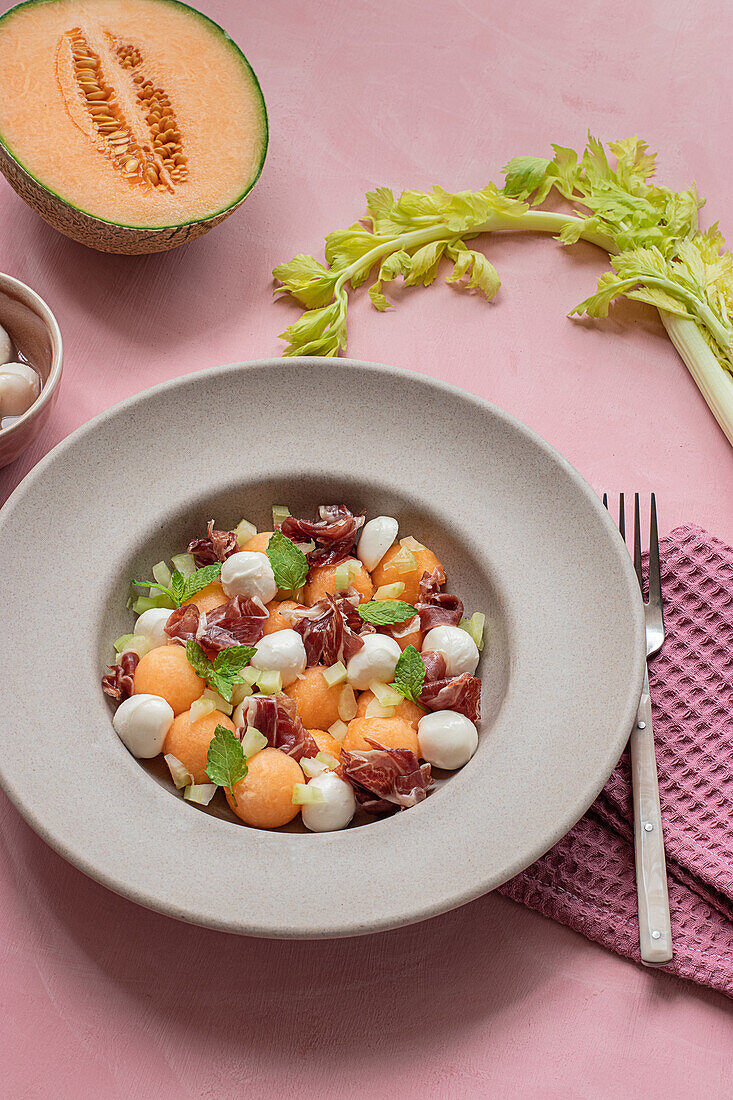 From above exotic melon, mozzarella and prosciutto salad on pink colorful background