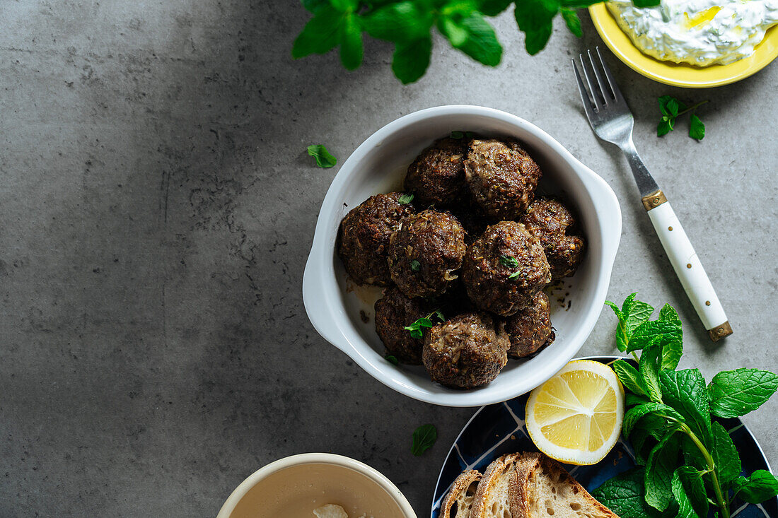 Top view of appetizing traditional homemade fried Greek meatballs served on gray background near plate with bread and lemon in kitchen