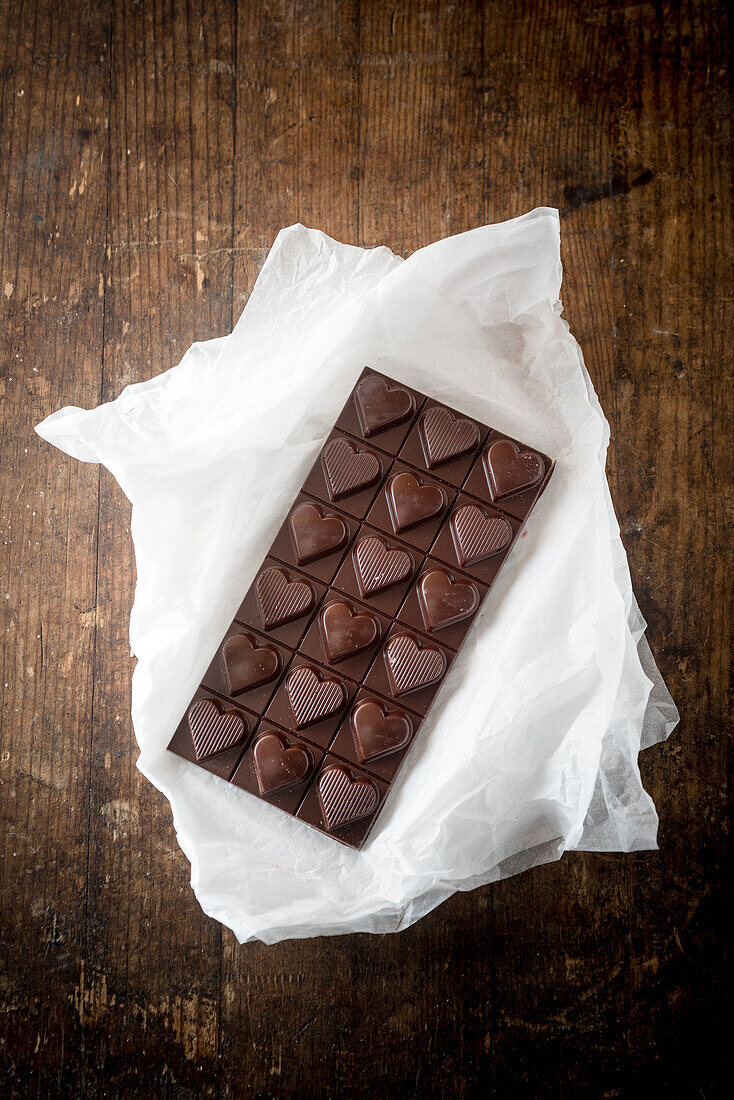 Top view of delicious candy chocolate bar in shape of heart on wooden table background