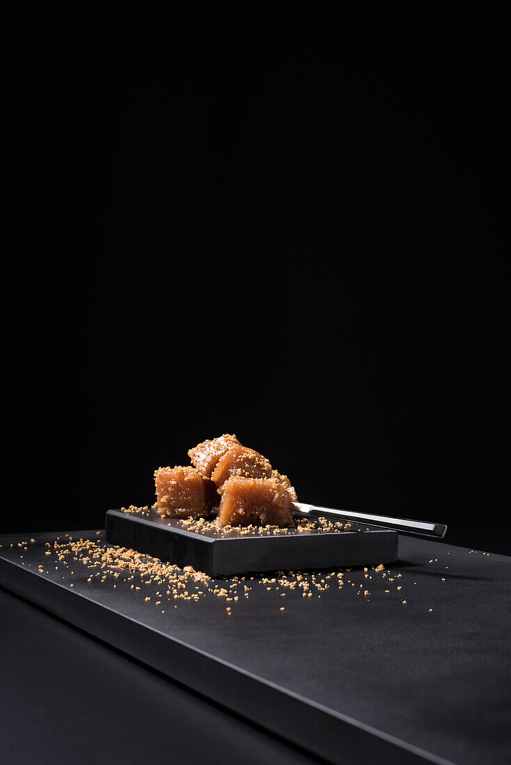 Gourmet quince jelly paste in ceramic plate sprinkled with sesame seeds on black background