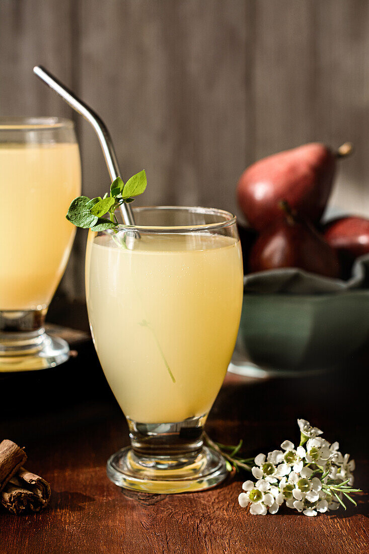 Glasses of delicious refreshing drinks with pear juice and fresh elderflower leaves on table with cinnamon sticks