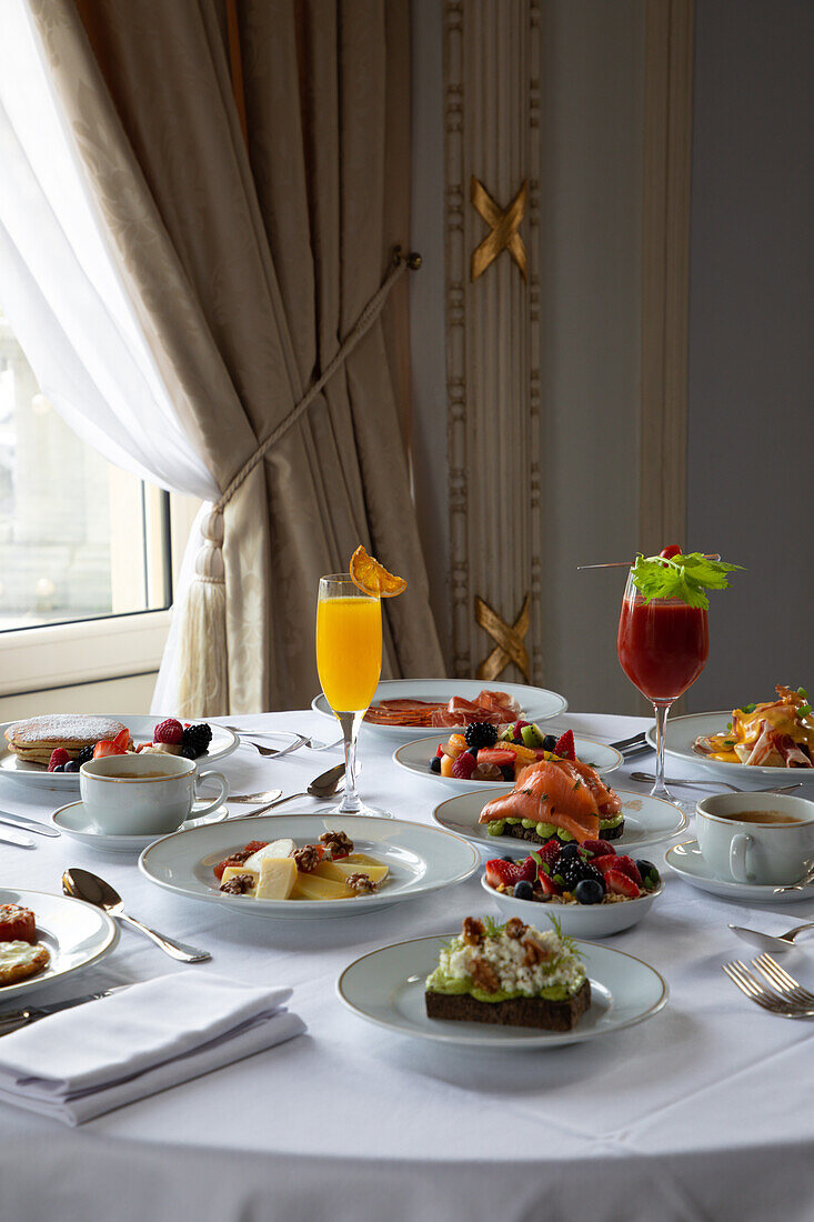 Various colorful dishes and juices served on round table during breakfast in elegant hotel restaurant in sunny morning