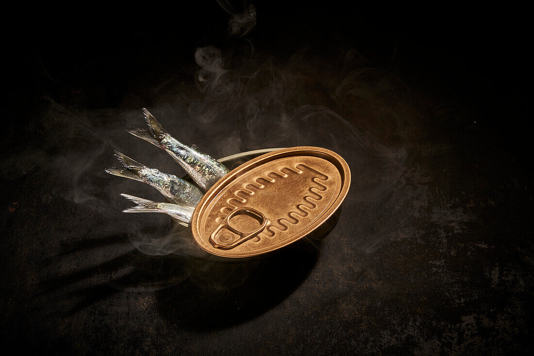 From above of canned fish in tin can with opened placed on black background with smoke in room with dim light