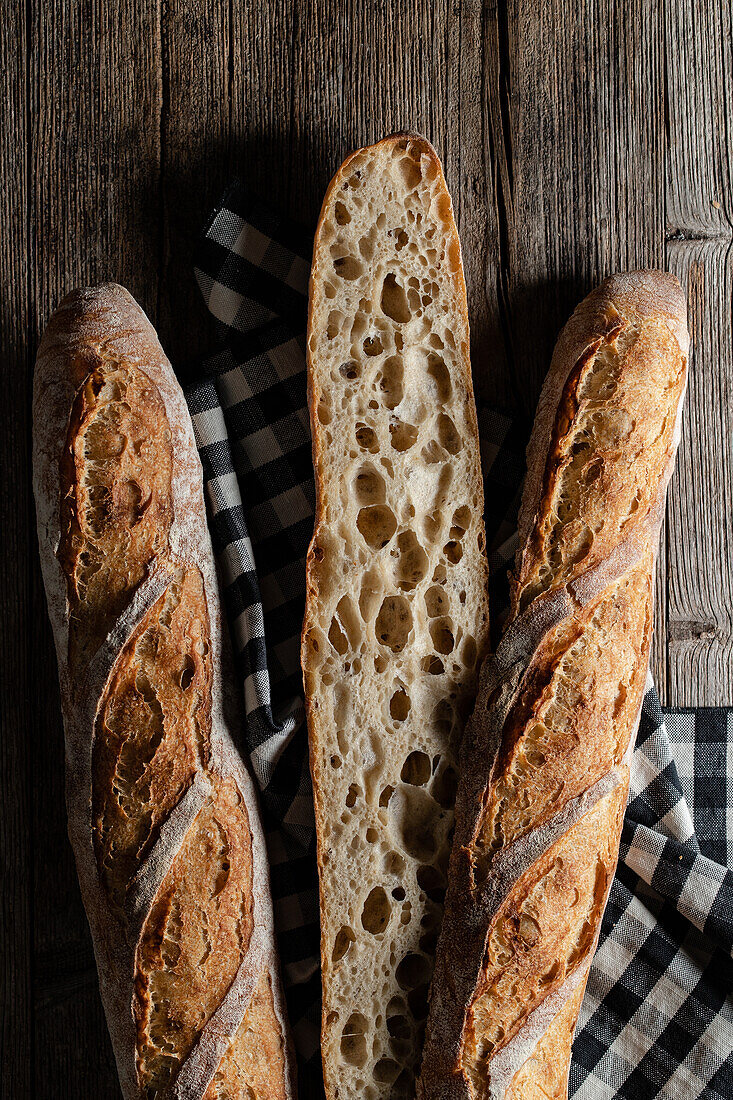 Top view of cut and whole sourdough baguettes with crunchy crust placed on wooden table