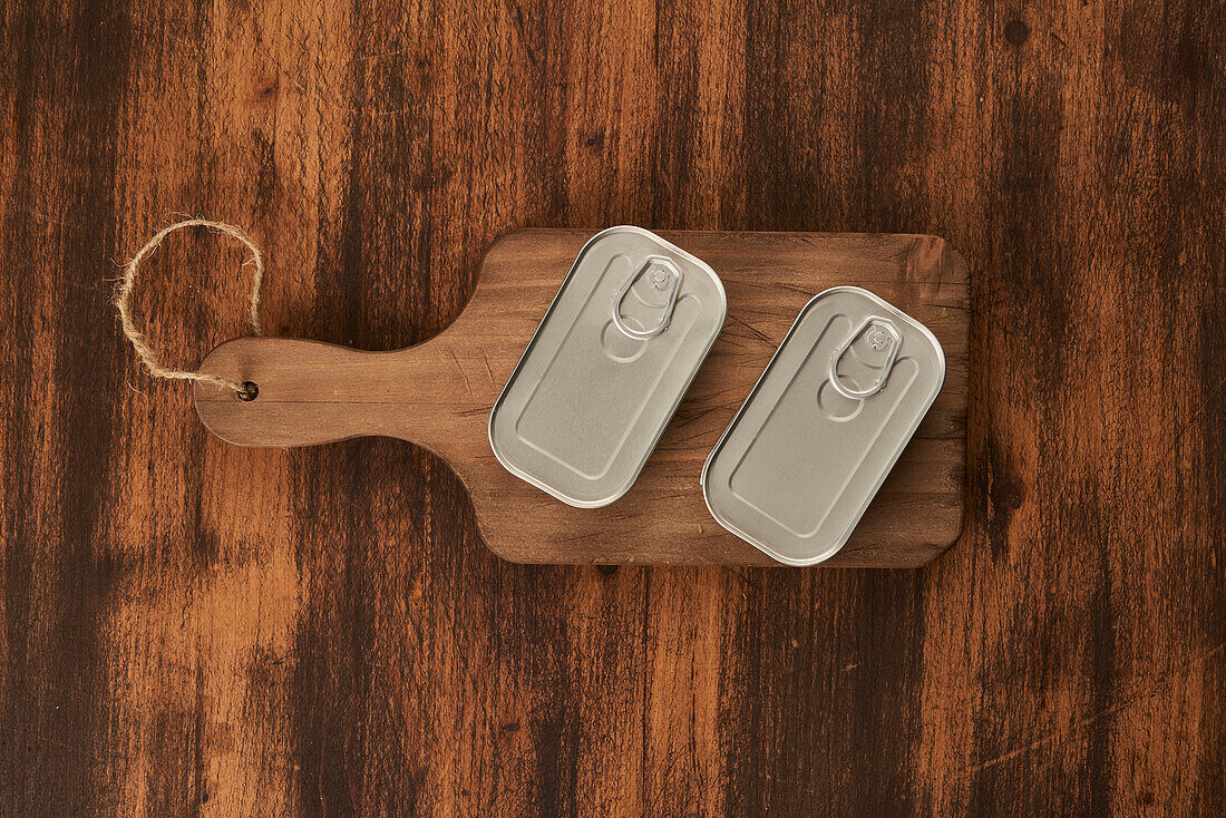 From above scratched chopping board with sealed cans with preserved food on rustic lumber table