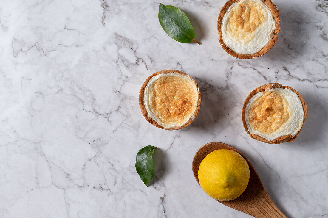 Top view of yummy homemade meringue tarts placed on table with fresh lemon and green leaves