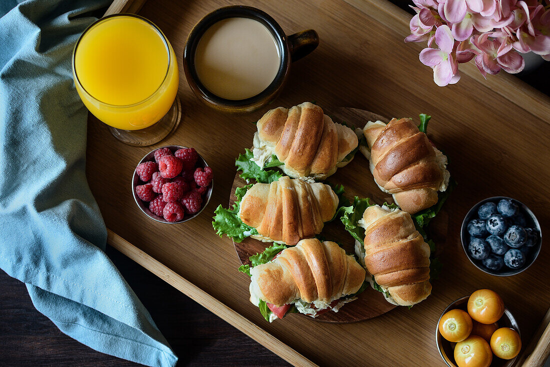 Delicious croissant sandwiches with vegetables served on tray with cappuccino and orange juice prepared for French breakfast and placed on wooden table