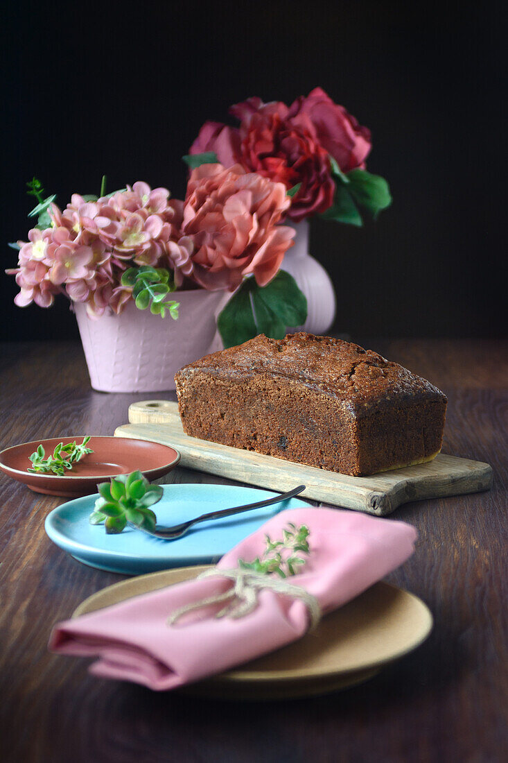 Still life of a sponge cake next to some pink vases with flowers on a table