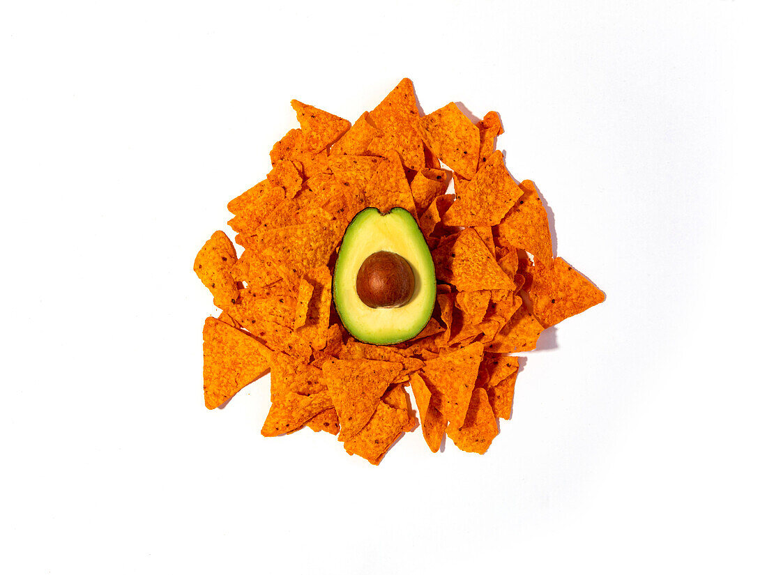 Top view of half of fresh avocado placed on pile of crunchy tortilla chips on white background