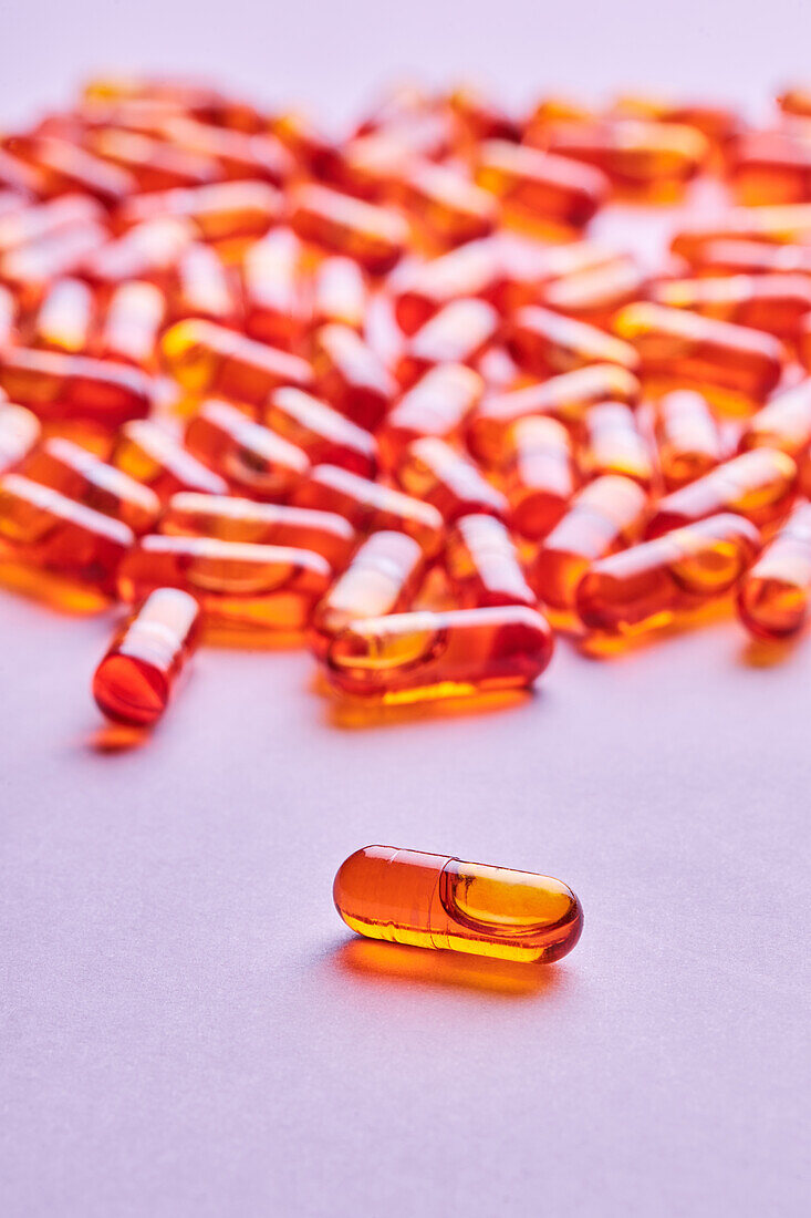 Composition of orange pills scattered on pink background in light studio