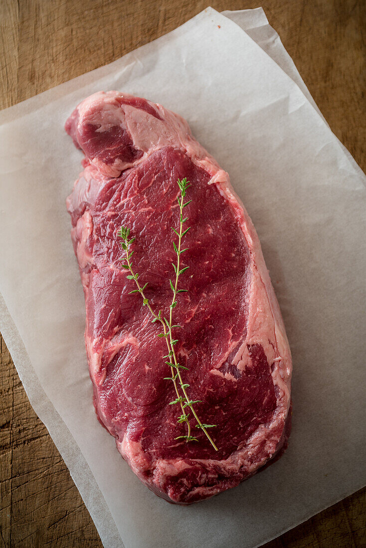 Overhead view of uncooked meat piece with thyme leaves against baking paper on brown background
