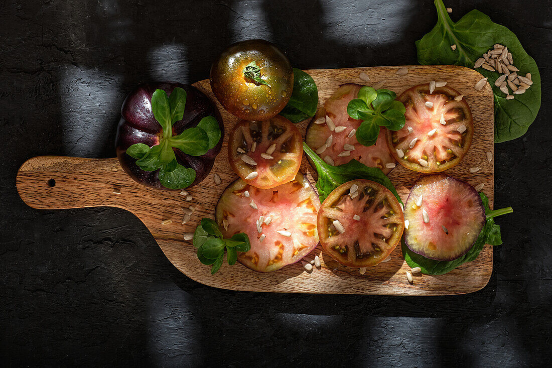 Top view of fresh ripe sliced black tomatoes and green mint stems on wooden cutting board on black background