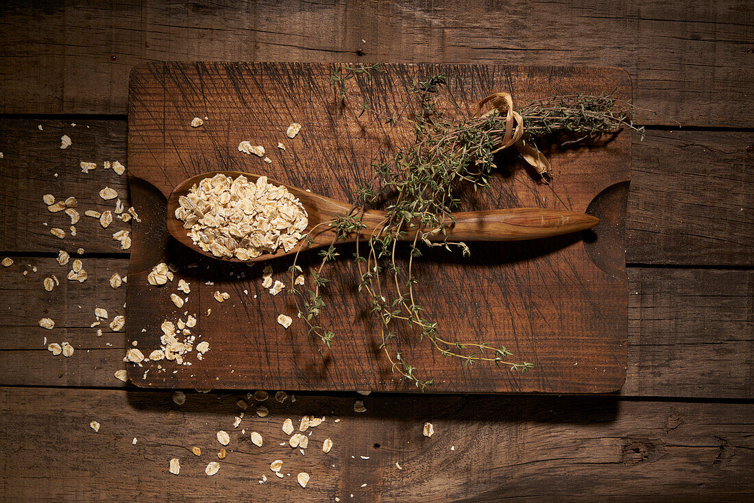 Top view composition with wooden spoon filled with healthy oatmeal flakes placed on cutting board on rustic plank table