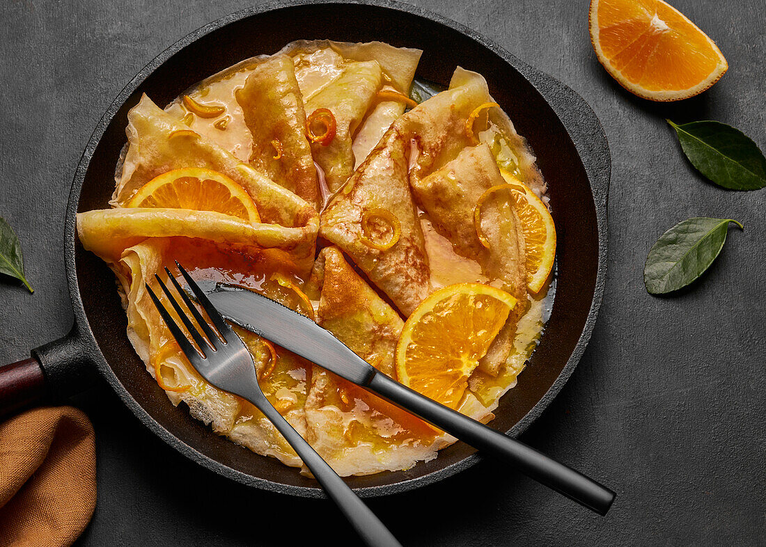 Von oben hausgemachte Crêpes Suzette mit Orangenlikör und Orangenscheiben auf einem Teller mit Messer und Gabel auf einer Betonfläche serviert