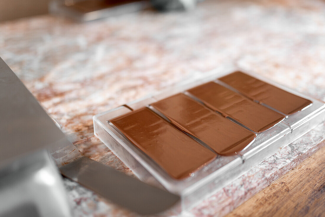 Soft focus of plastic molds with bars of handmade chocolate placed on table in confectionery